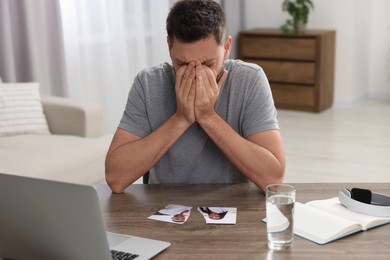 Photo of Crying man with parts of photo sitting at table indoors. Divorce concept
