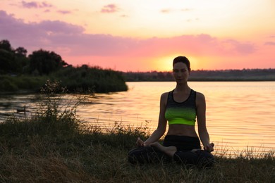 Photo of Mature woman meditating near river at sunset. Space for text