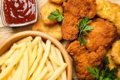 Photo of Tasty deep fried chicken pieces and nuggets with garnish on table, top view