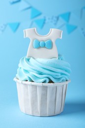 Photo of Beautifully decorated baby shower cupcake with cream and boy topper on light blue background