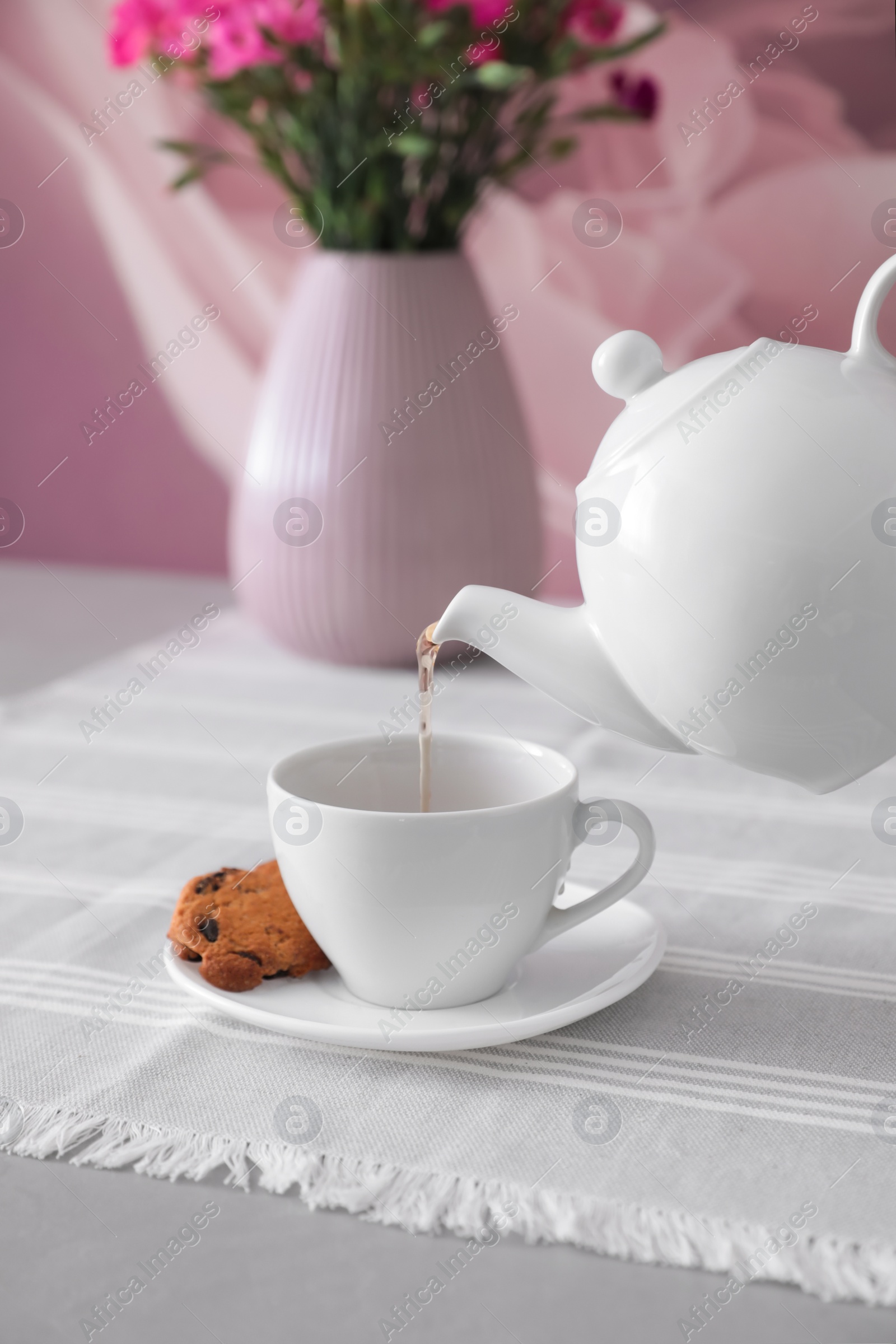 Photo of Pouring hot tea into ceramic cup on table