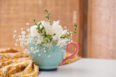 Photo of Beautiful bright flowers in cup and fabric on white table indoors. Space for text