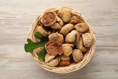 Photo of Wicker basket with tasty dried figs and green leaf on light wooden table, top view