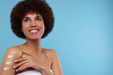 Photo of Beautiful young woman applying body cream onto arm on light blue background, space for text