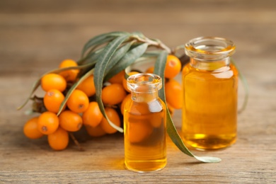 Photo of Natural sea buckthorn oil and fresh berries on wooden table