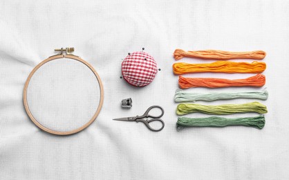 Photo of Flat lay composition with threads and embroidery hoop on white fabric