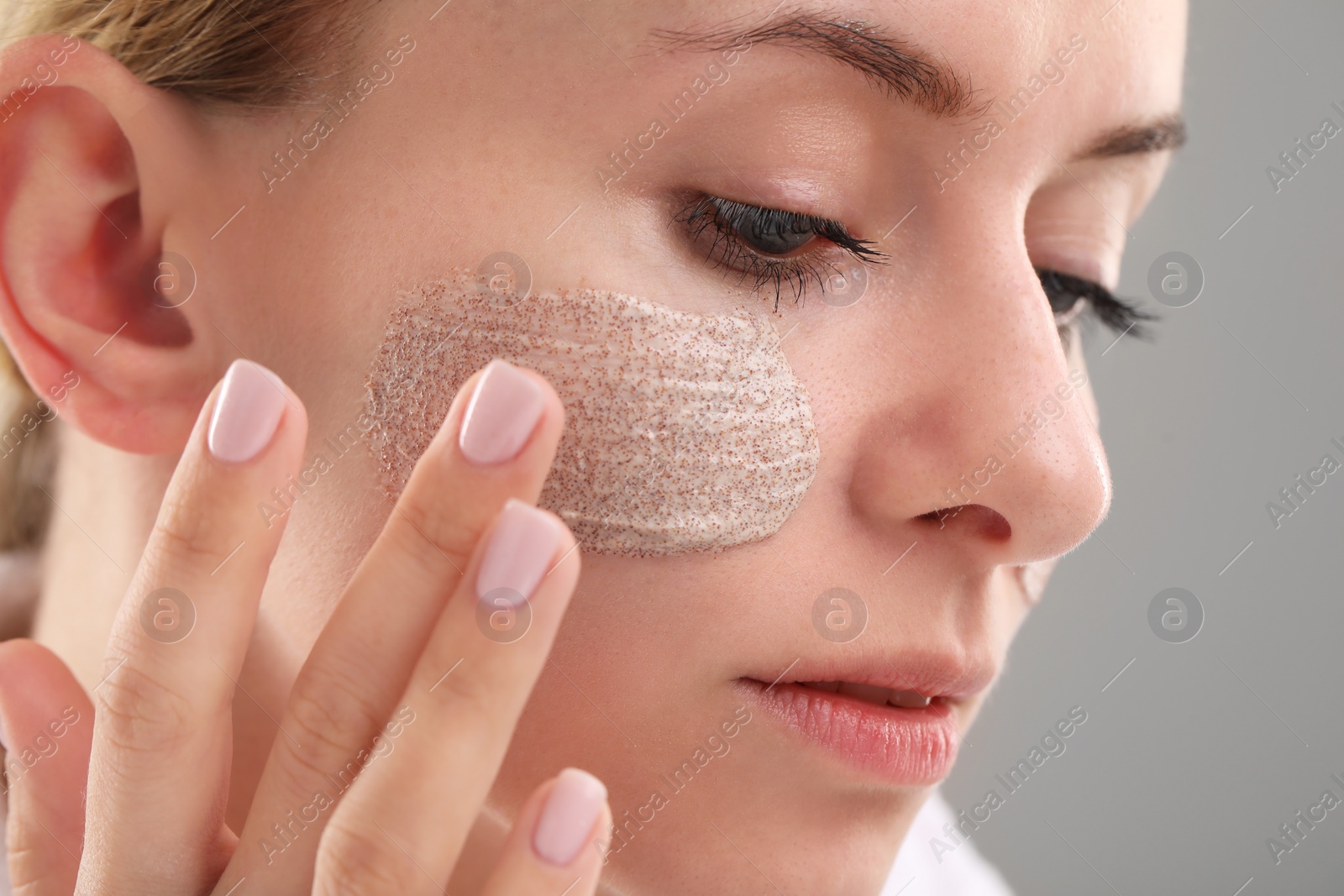 Photo of Woman applying cosmetic product on her face against grey background, closeup. Spa treatments