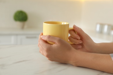 Photo of Woman with yellow cup at table indoors, closeup