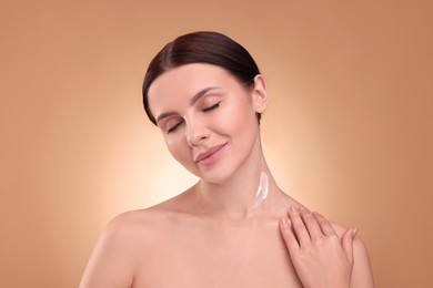 Photo of Beautiful woman with smear of body cream on her neck against light brown background