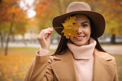 Young woman in stylish clothes holding yellow leaf outdoors. Autumn look