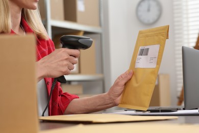 Photo of Seller with scanner reading parcel barcode at table in office, closeup. Online store