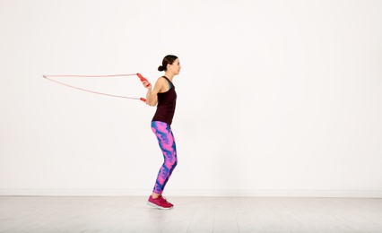 Photo of Young sportive woman training with jump rope in light room