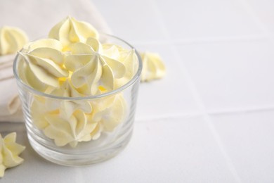 Photo of Tasty meringue cookies in glass on white tiled table. Space for text