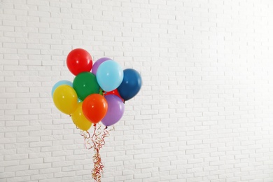 Photo of Bunch of bright balloons near brick wall, space for text. Celebration time
