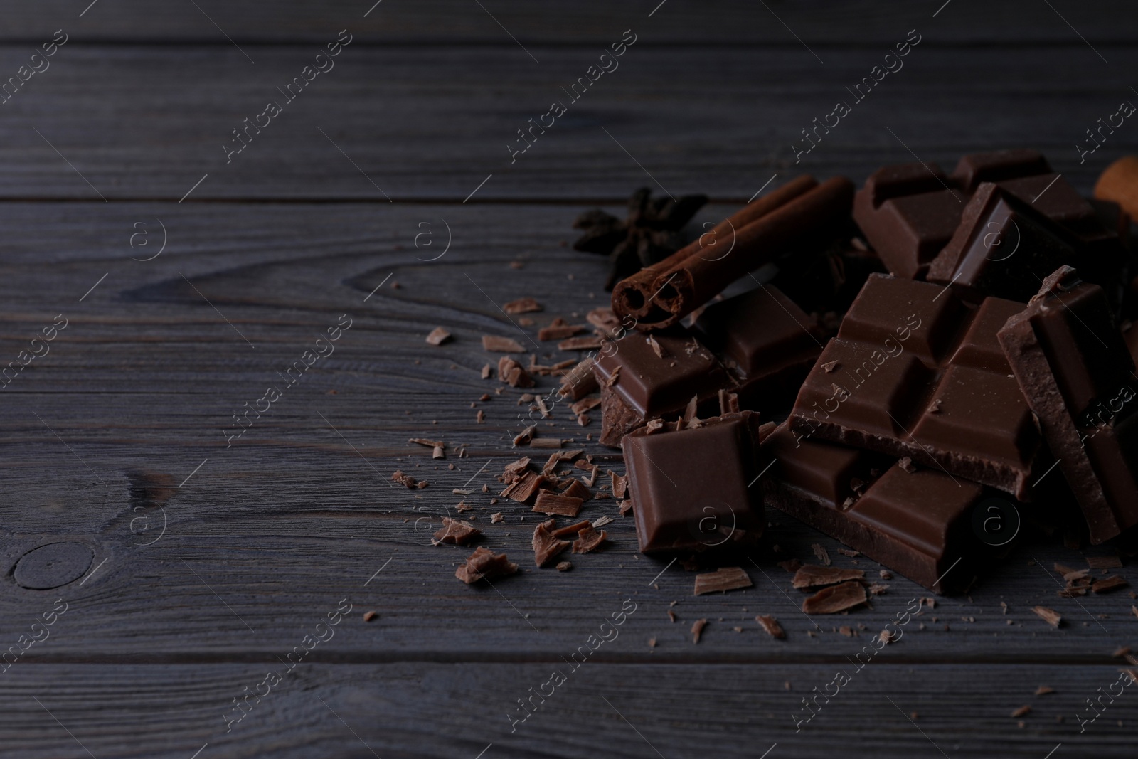 Photo of Delicious milk chocolate and cinnamon on wooden table. Space for text