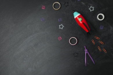Photo of Bright toy rocket and school supplies on chalkboard, flat lay. Space for text