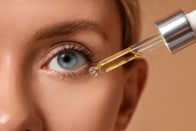 Photo of Woman applying cosmetic serum onto her face on beige background, closeup