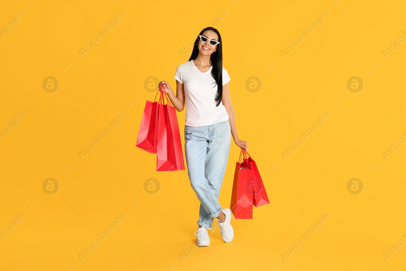 Photo of Beautiful young woman with paper shopping bags on yellow background