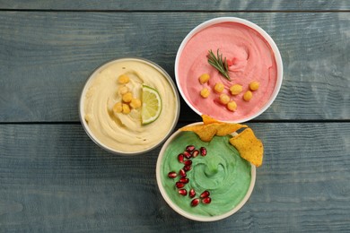 Photo of Different kinds of tasty hummus served with nachos on light blue wooden table, flat lay