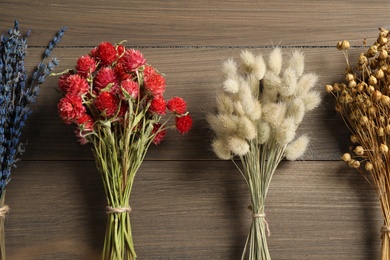 Photo of Bunches of beautiful dried on wooden table, flat lay