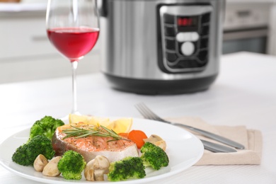 Photo of Plate with salmon steak and garnish prepared in multi cooker on table