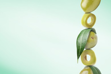 Image of Cut and whole green olives with leaves on light turquoise gradient background, space for text