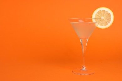 Photo of Martini glass of refreshing cocktail with lemon slice on orange background, space for text