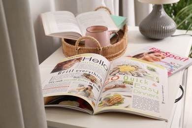 Photo of Different lifestyle magazines, books and coffee on chest of drawers indoors