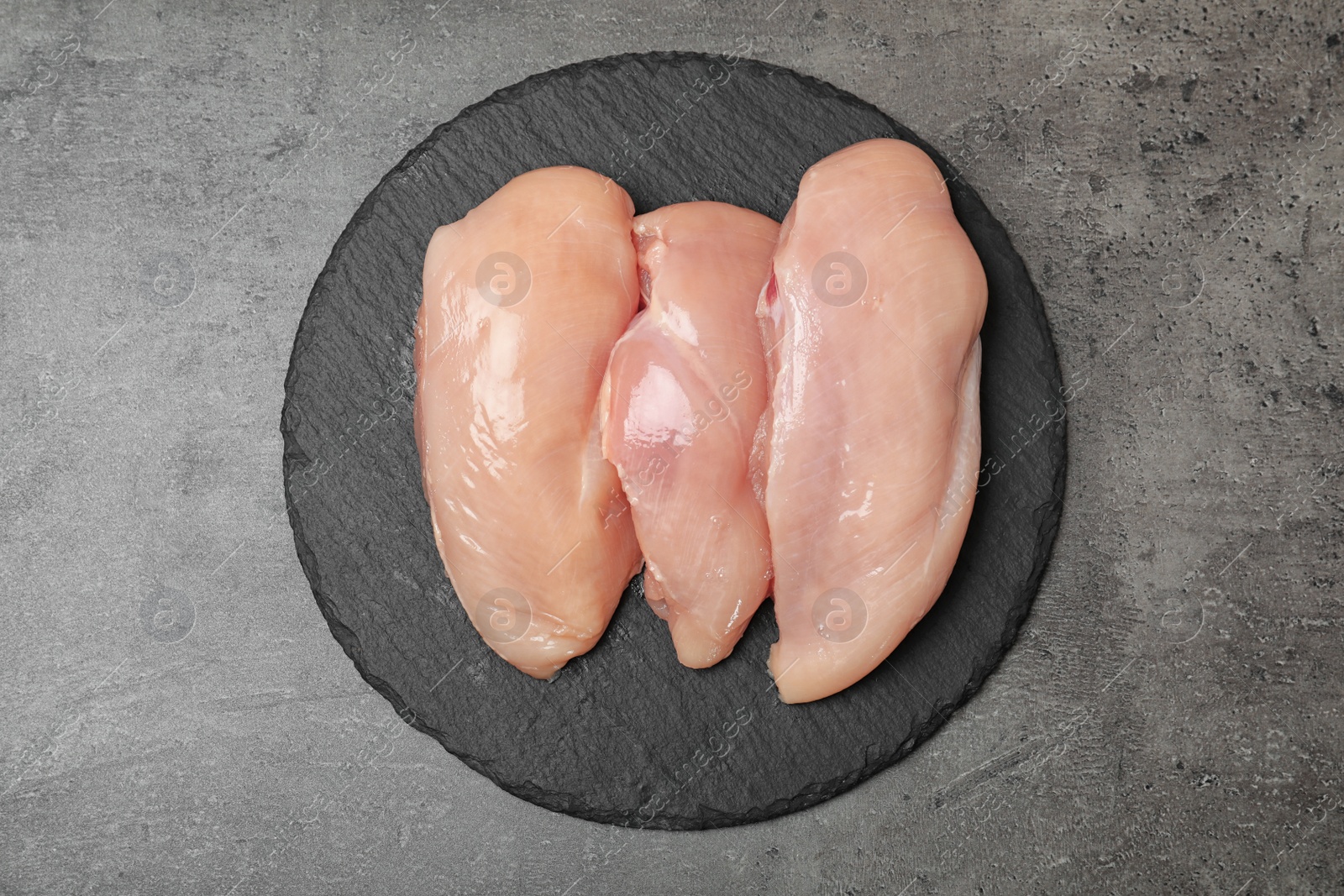 Photo of Slate plate with raw chicken breasts on grey background, top view. Fresh meat