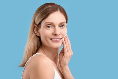 Photo of Beautiful woman removing makeup with cotton pad on light blue background, space for text