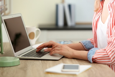 Photo of Young woman using laptop at table indoors, closeup. Space for text