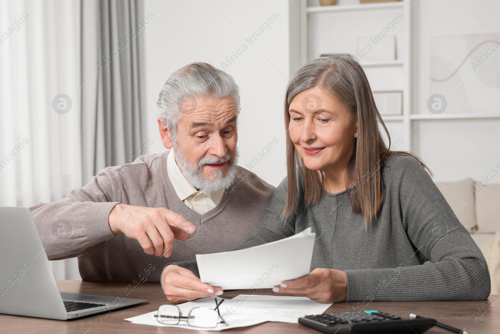 Photo of Elderly couple with papers and laptop discussing pension plan at wooden table in room