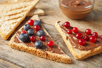 Photo of Slices of bread with chocolate paste and berries on wooden table