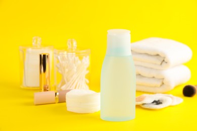 Photo of Dirty cotton pads, lipstick, toiletries and makeup removal product on yellow background