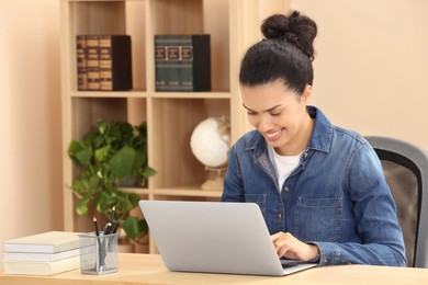 Photo of African American woman typing on laptop at wooden table indoors