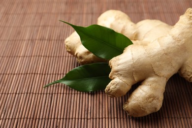 Photo of Fresh ginger with leaves on bamboo mat, closeup. Space for text