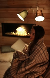Photo of Young woman resting near decorative fireplace at home. Winter season