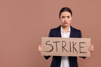 Photo of Upset young woman holding cardboard banner with word Strike on brown background, space for text