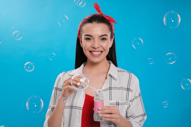 Photo of Young woman blowing soap bubbles on light blue background