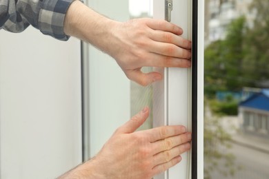 Photo of Worker putting rubber draught strip onto window indoors, closeup