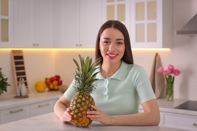 Photo of Young woman with fresh pineapple in kitchen. Exotic fruit