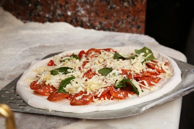 Photo of Peel with raw traditional Italian pizza on table in restaurant kitchen
