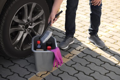 Photo of Man taking brush from bucket with car cleaning products outdoors, closeup
