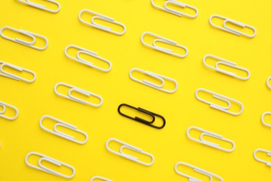 Photo of Black paper clip among white ones on yellow background, flat lay. Concept of racism