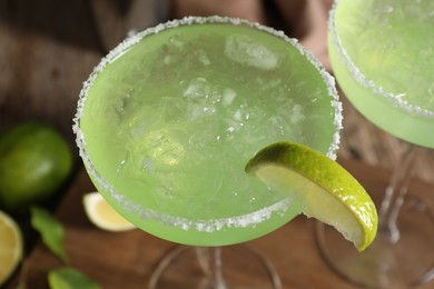 Photo of Delicious Margarita cocktail with ice cubes in glasses and lime on table, closeup