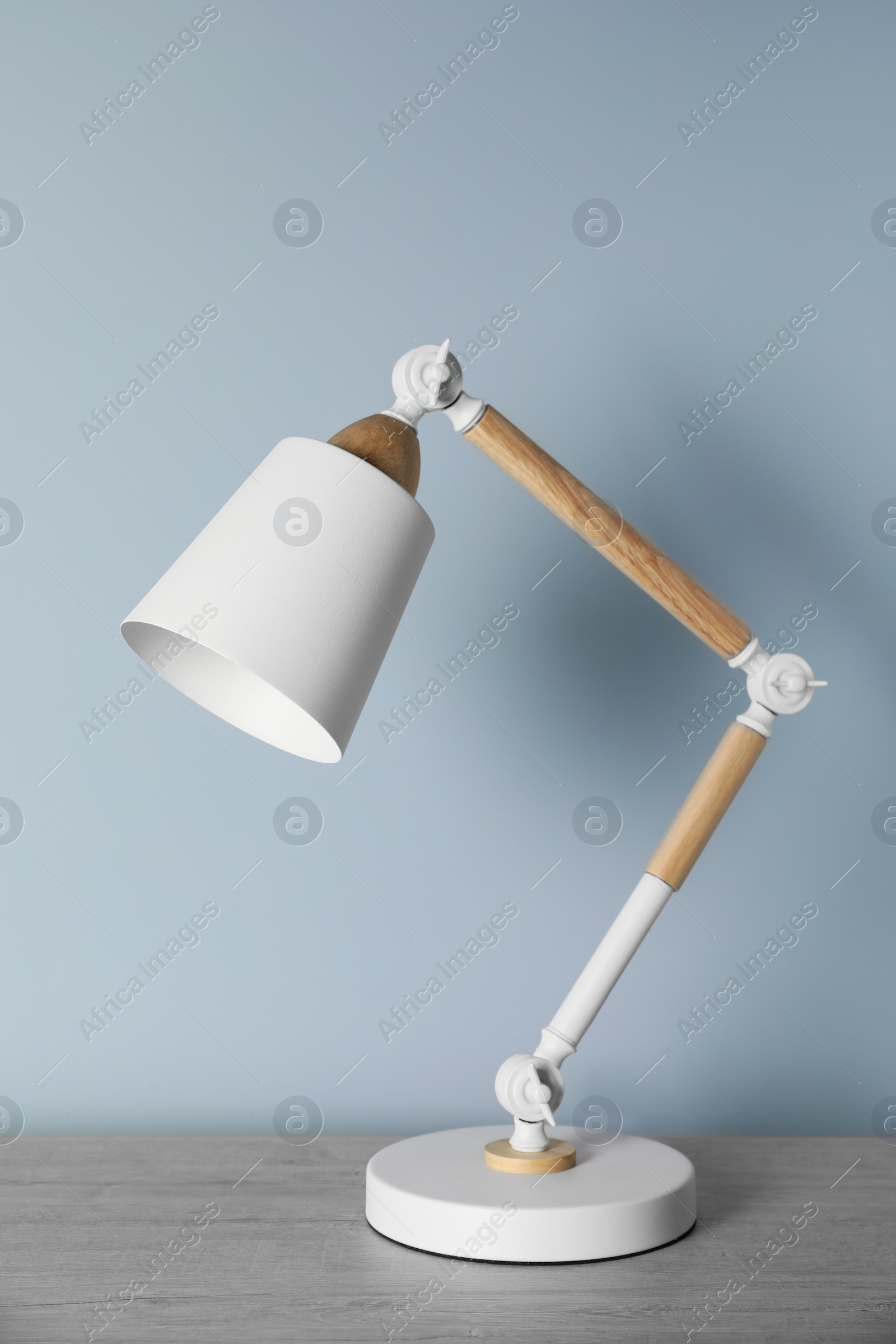 Stylish modern desk lamp on wooden table near white wall Photo of Stylish modern desk lamp on wooden table near white wall