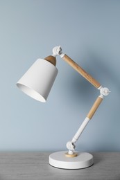 Photo of Stylish modern desk lamp on wooden table near white wall