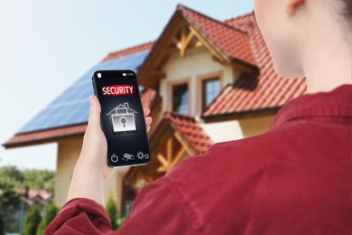 Image of Woman using home security system application on smartphone outdoors, closeup
