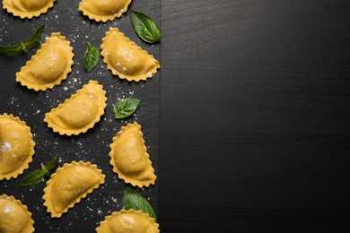 Photo of Raw ravioli with basil on black table, flat lay and space for text. Italian pasta