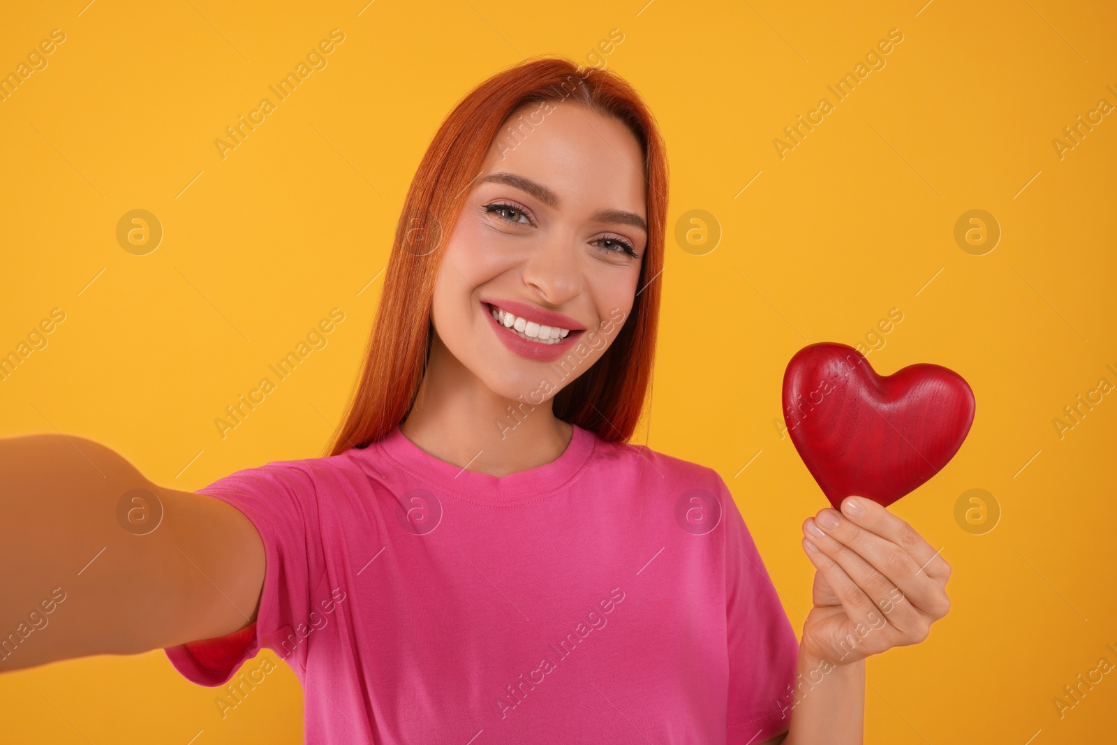 Photo of Beautiful happy woman with red heart taking selfie on orange background